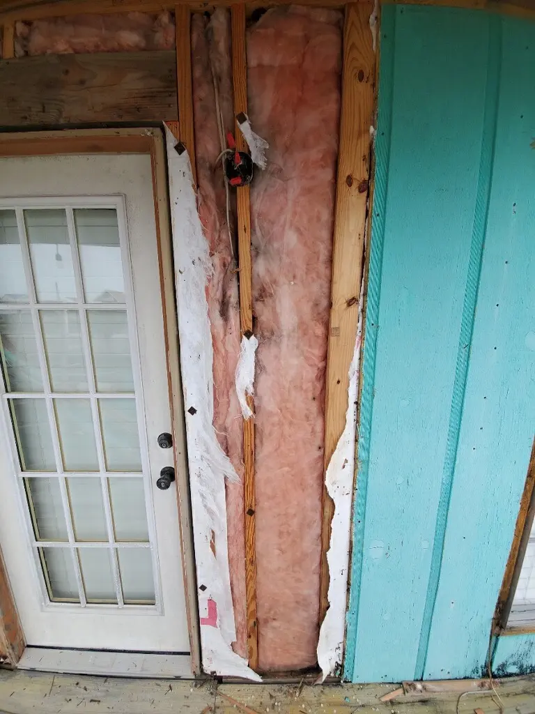 Exposed wall studs and pink insulation beside an exterior door at The Alibi.