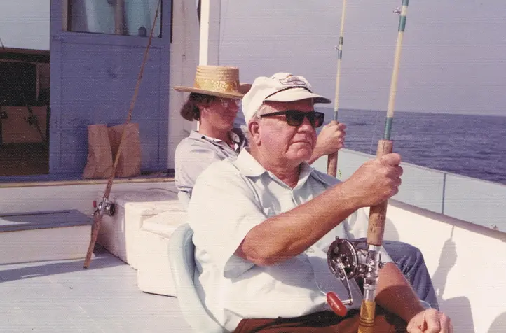 Clem Binnings seated aboard a boat with fishing rods and open water behind him.