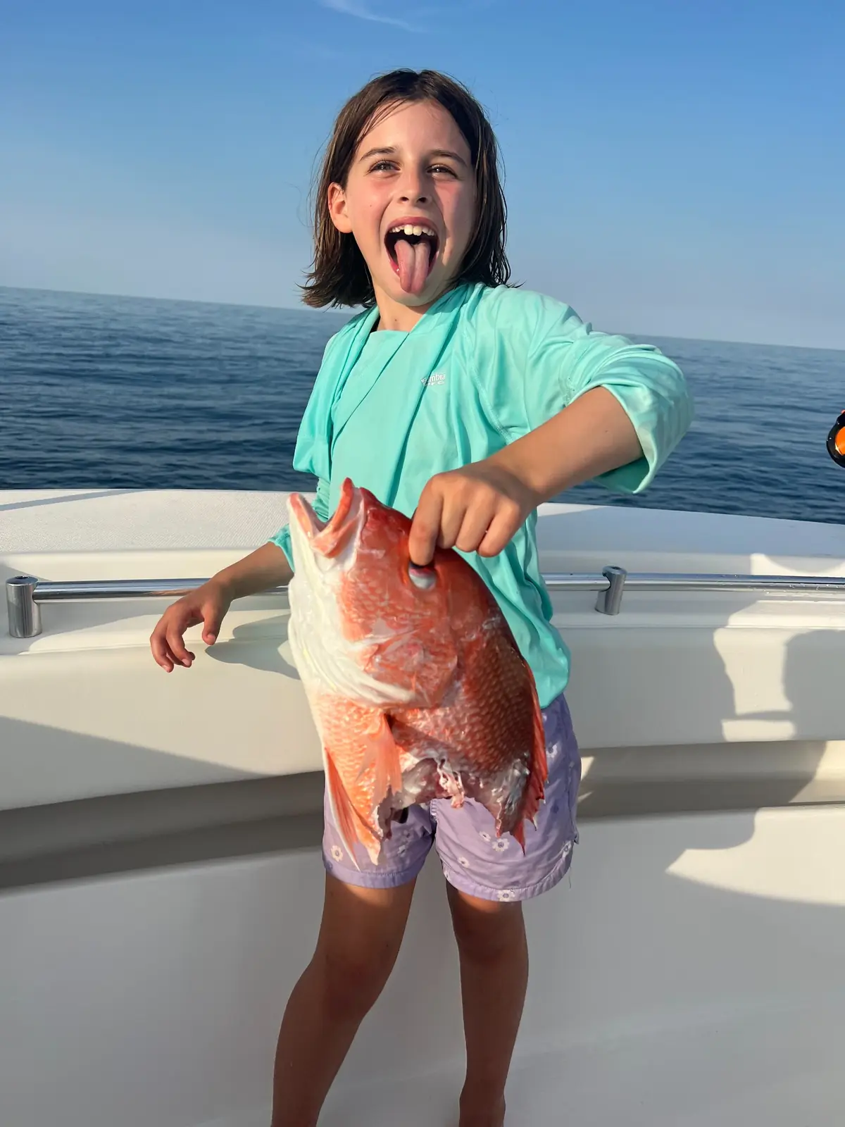 A smiling child holds a red snapper aboard a fishing boat.